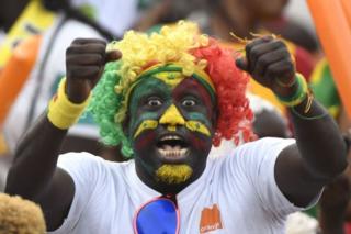 A Senegal supporter whose face is painted in the colours of the country's flag cheers ahead of the match.