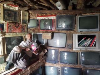   A man reads in his house near the wall in which the televisions are built 