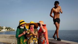 A man walks by as tourists take selfies on the French Riviera city of Nice on June 24, 2019, as temperatures soar to 33 degrees Celsius