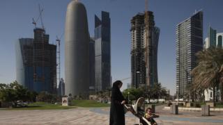 A woman pushes a pram near new office skyscrapers in the financial district in Doha,