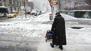 Idosa atravessa a rua em meio a neve