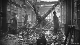 Мужчины смотрят на книги в поврежденной бомбой библиотеке