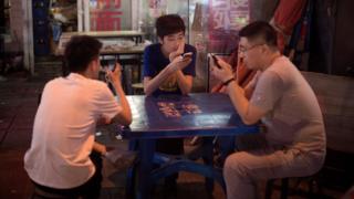 Трое мужчин сидят за столом и смотрят на свои телефоны