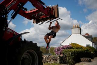 An athlete uses a piece of farm machinery to do pull-ups on