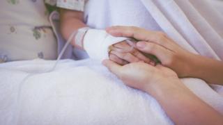 Mão de adulto segura a mão de uma criança hospitalizada