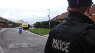 The back of a PSNI officer facing a cordoned off area with a police van visible