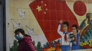 A woman wears a mask as she passes a propaganda mural in Beijing, China. Photo: 8 February 2020