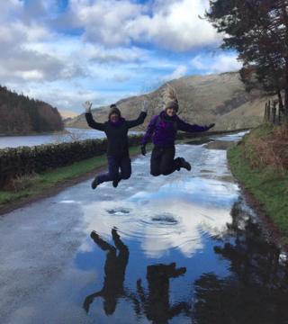 Two people jumping over a puddle of water