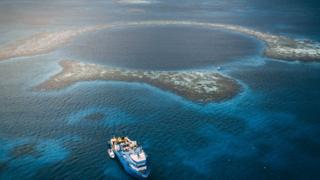 Vista aérea do Buraco Azul de Belize - um círculo azul escuro no meio do mar, cercado por recifes