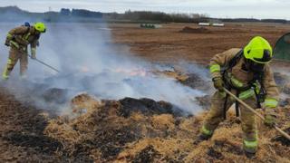 Two firefighters prodding burning hay with a long stick