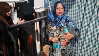 A Palestinian woman holds bottles filled with water