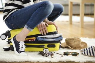 woman sitting on a yellow suitcase, trying to close it
