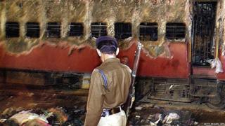 28 February 2002, an Indian policeman looks towards a burnt train coach and belongings of Hindu activists at Godhra Railway Station.