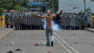 Демонстранты жесты перед венесуэльскими национальными полицейскими, стоящими на страже у международного моста Симона Боливара в Кукуте