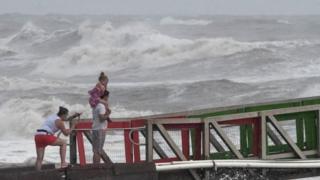 A girl covers her face from strong winds as her family members watch high swells from Hurricane Hanna from a jetty in Galveston, Texas