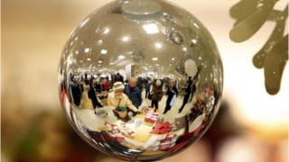 Christmas shoppers in John Lewis reflected through a glass ball