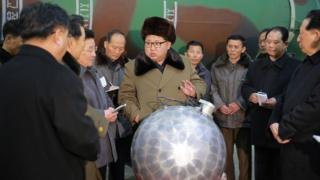 Kim Jong-Un talking with scientists and technicians alongside a mock-up of a nuclear bomb