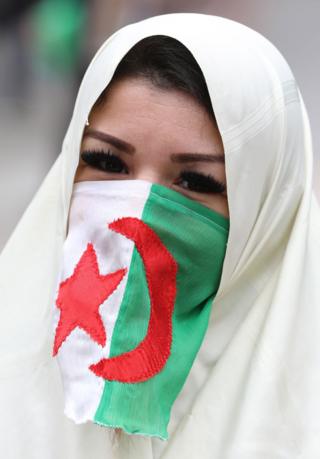 A woman in a hijab and an Algerian flag covering her nose and mouth