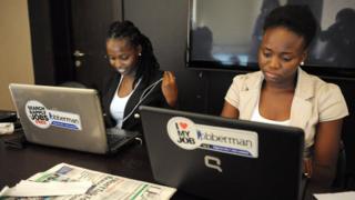 Two women dey look computer