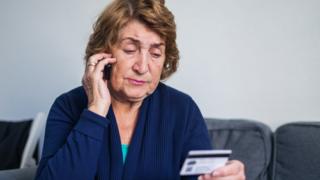 Idosa segura um cartão enqianto fala ao telefone