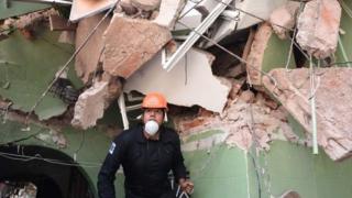 Homem de capacete e máscara anda em meio a escombros