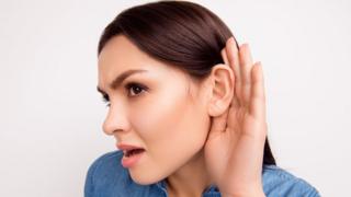 Mujer joven con mano en la oreja.