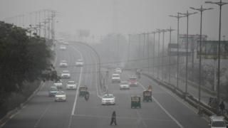 An Indian woman crosses a road as vehicles move through morning smog on the last day of a two-week experiment to reduce the number of cars to fight pollution in New Delhi, India, Friday, Jan. 15, 2016