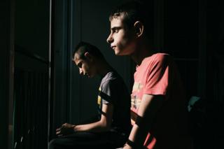 Two twin boys sit indoors next to a window