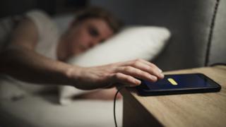 A person putting mobile beside the bed
