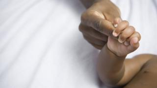 Mão de bebê aperta dedo de um adulto
