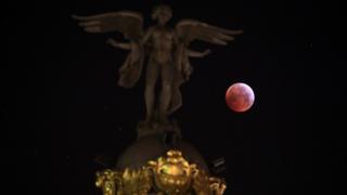 The moon is seen beside "Victoria Alada" statue on the top of Metropoli building during a total lunar eclipse, known as the "Super Blood Wolf Moon" in Madrid, Spain