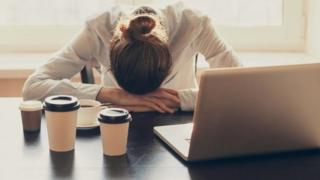 سيدة تضع رأسها على مكتب العمل وأمامها جهاز كمبيوتر محمول