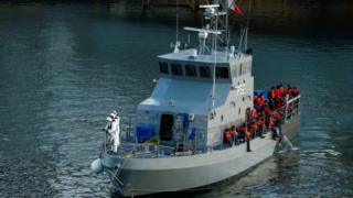 Rescued migrants are seen on an Armed Forces of Malta vessel after arriving in Valletta's Grand Harbour