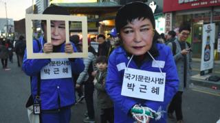 Протестующие одеты в качестве лидера Пак Гуэн Хе в масках и тюремной форме во время митинга в декабре 2016 года