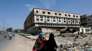 Women walk along a road with an abandoned building of a garment factory in the background, where over 260 people were killed after a fire broke in 2012, in Karachi, Pakistan September 17, 2020.