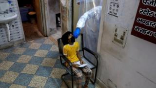 Um profissional de saúde em equipamento de proteção individual coleta uma amostra usando um cotonete de uma menina em um centro de saúde para realizar testes em Delhi, 27 de junho