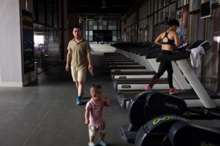 Huang Wensi's husband, Deng Peipeng, takes care of their son while accompanying him for a workout in a local gym
