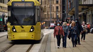 Shoppers wearing masks walk beside a tram route in Manchester city centre