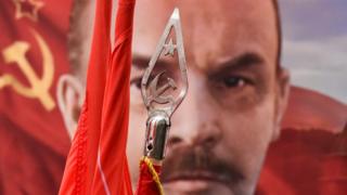 A photo of Vladimir Lenin behind a banner showing the communist symbol