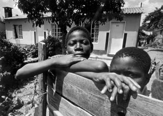 Молодые родезийские мальчики позируют за забором в январе 1977 года в Солсбери, Родезия и бывшей столице Зимбабве. Правительство Родезии и черные националисты сталкиваются с длинной партизанской борьбой, что привело к соглашению и созданию многорасовой новой Ассамблеи в 1978 году. В 1980 году британское правительство провозгласило независимость Южной Родезии, став Зимбабве. Роберт Мугабе назначен премьер-министром.
