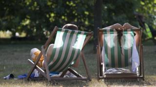 Пара отдыхает на шезлонгах в теплую погоду в Гайд-парке