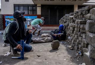 Masked youths with homemade mortars take cover behind a barricade as police bullets fly overhead