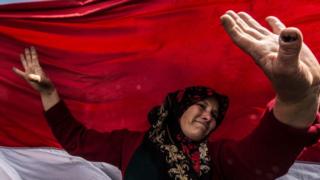 An Egyptian woman dances before a large national flag in Cairo's northern suburb of Shubra al-Khaymah on the second day of voting in the 2018 presidential elections on 27 March.