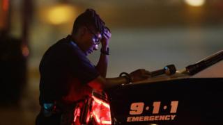 Офицер полиции Далласа, который не хотел, чтобы его опознали, занимает минуту, когда она охраняет перекресток рано утром после стрельбы в центре Далласа, пятница, 8 июля 2016 г.