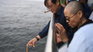 Liu Xiaobo's wife Liu Xia (R) prays as his ashes are scattered in the sea near Dalian