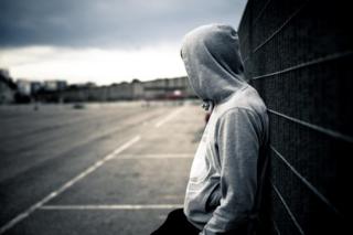 Teenager in hood leans on railing