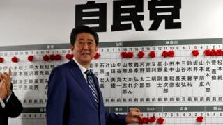 安倍晋三在自民党总部的当选名录前朝着记者咧嘴而笑(22/10/2017)