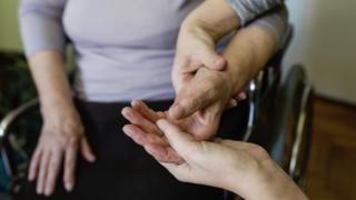 Una terapeuta manipula la mano de una mujer en silla de ruedas