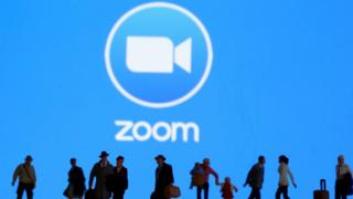 Small toy figures are seen in front of displayed Zoom logo in this illustration taken.