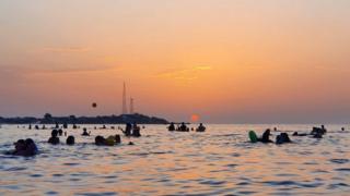 People bathe in the Mediterranean sea water off a beach in Libya's capital Tripoli near sunset on August 18, 2020.